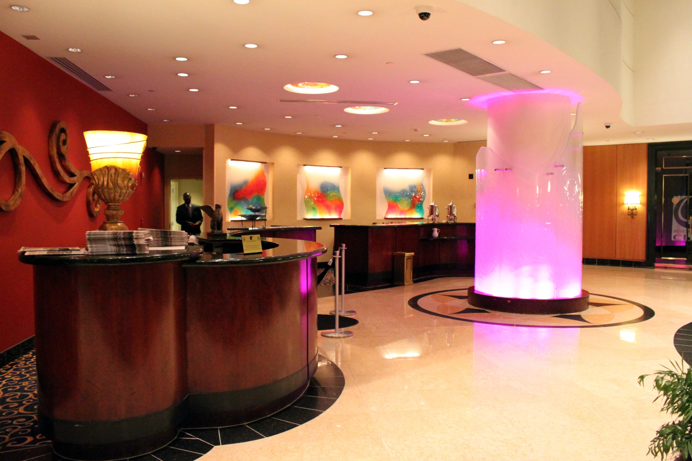 a brightly lit reception area features round counter and circular red column with pink lights