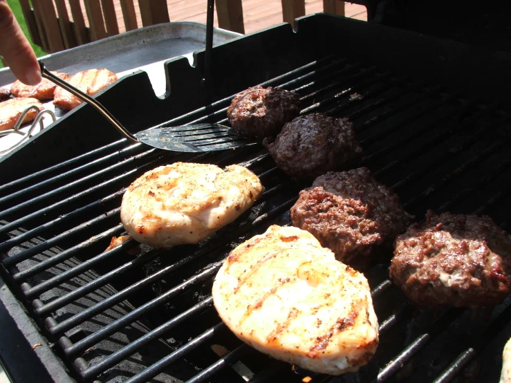 a person is cooking hamburgers and hamburger patties on an outdoor grill