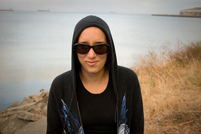 a lady in sunglasses is standing by the water