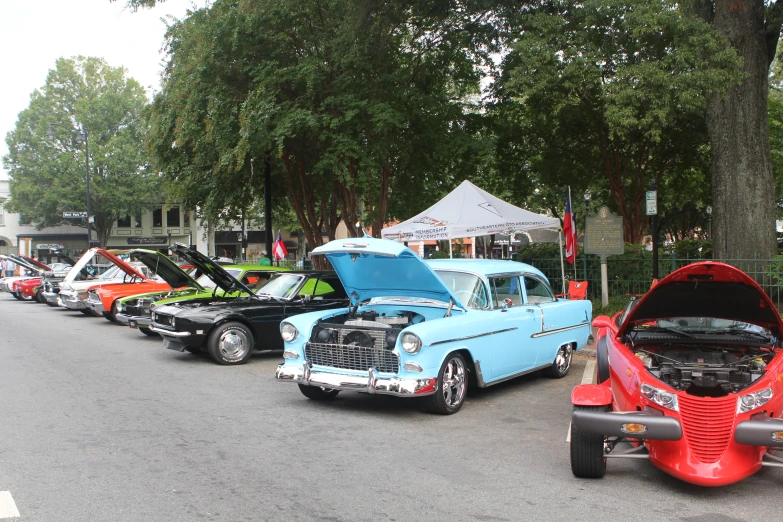 several cars with their hoods open, lined up at a car show