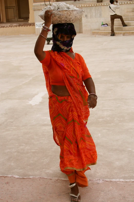 a woman in an orange outfit carrying soing up on her head