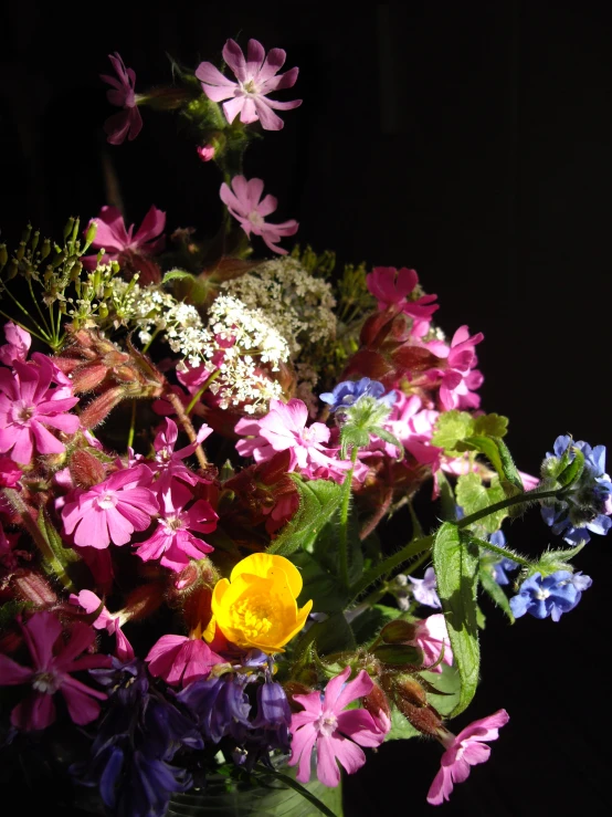 a green vase filled with purple and yellow flowers