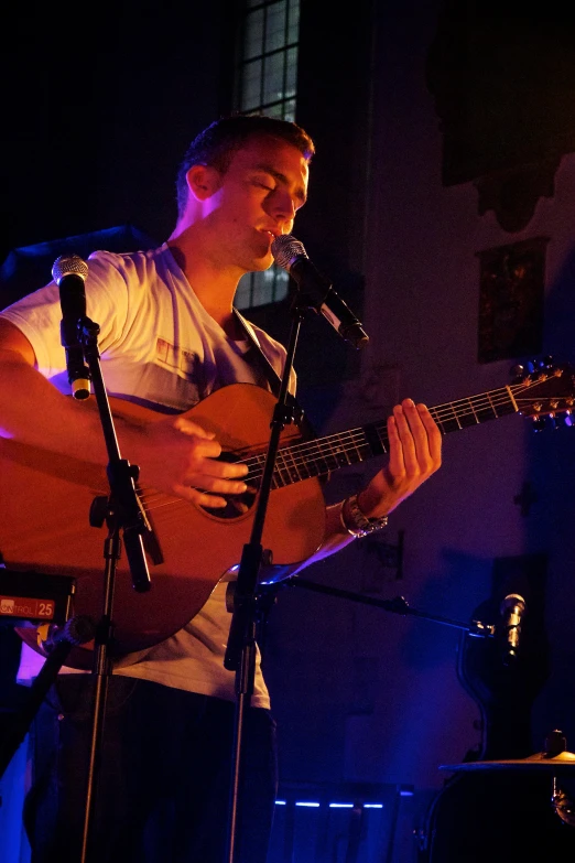 a man playing guitar and singing into microphones