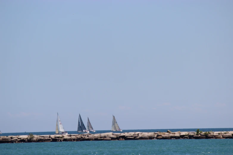 several sailboats sailing in the water off a pier