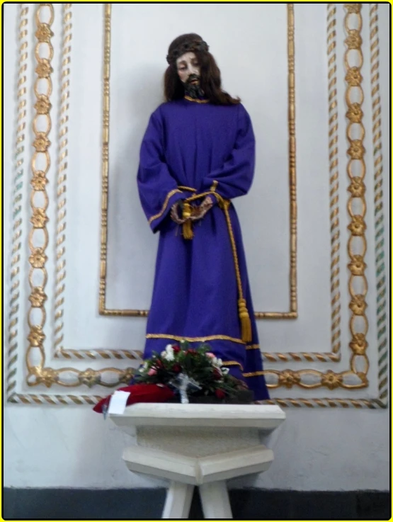 a statue of jesus wearing a robe and a christmas wreath in front of an ornate wall