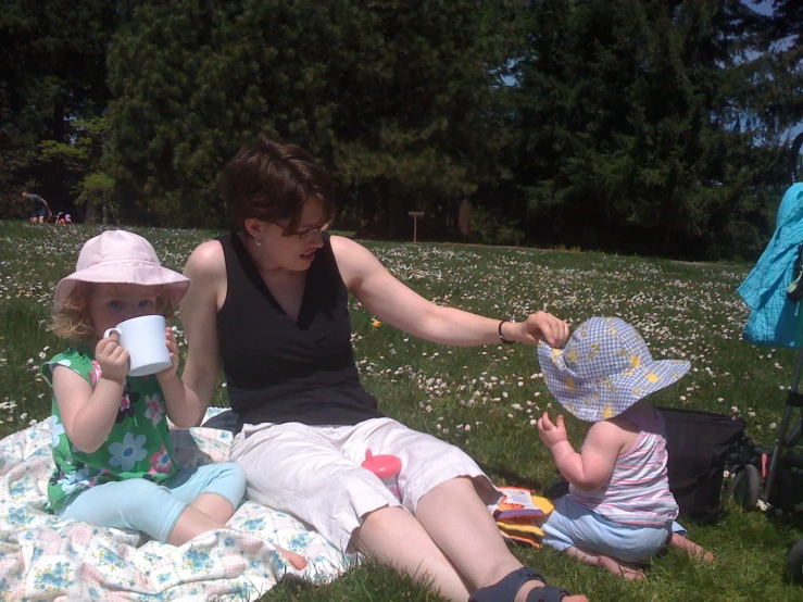 a woman holding a paper cup with two children sitting on a blanket