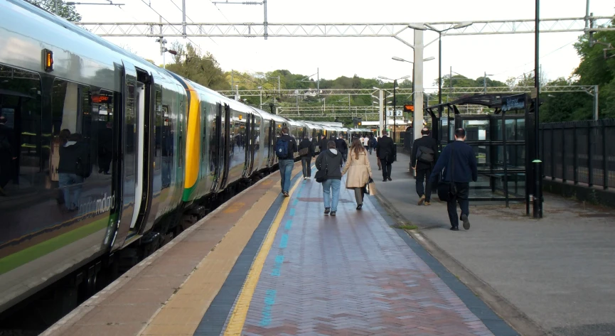 people walking beside and off a train as it is pulling into a station