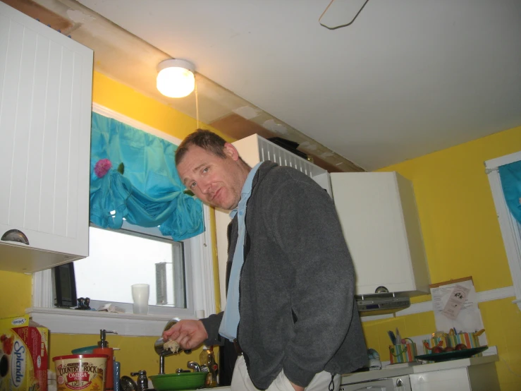 a man standing in a kitchen by a window with a handbag