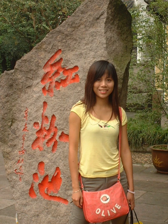 a woman holding a yellow bag standing next to a big rock