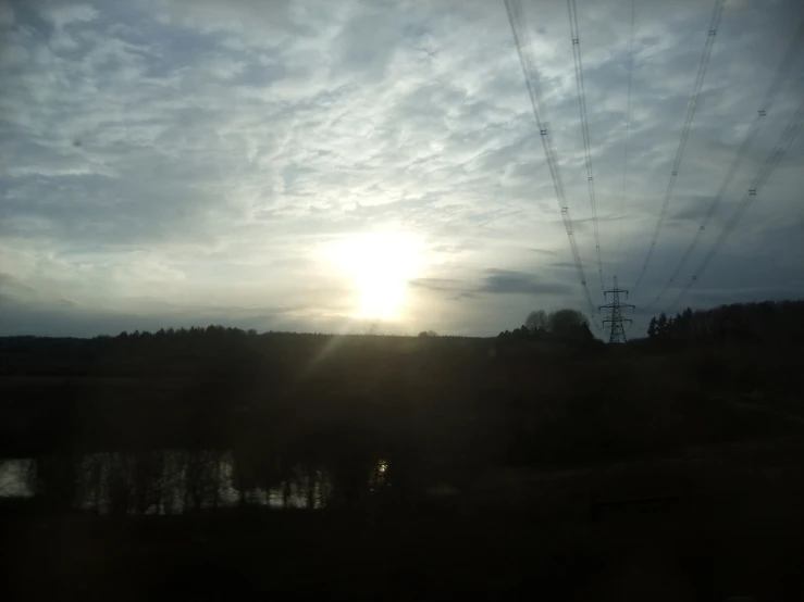the sun rises over a lake and power lines