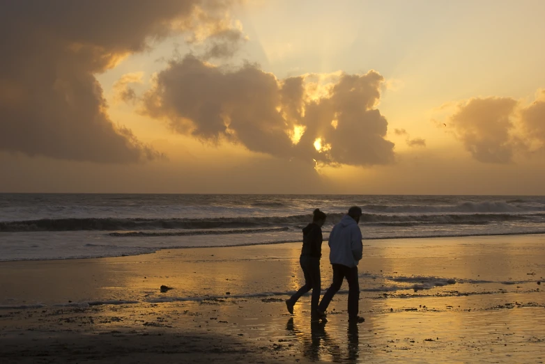 two people standing on the beach and one is walking away from the water