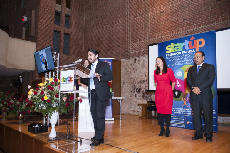 a man in a suit stands at a podium as two woman stand beside him