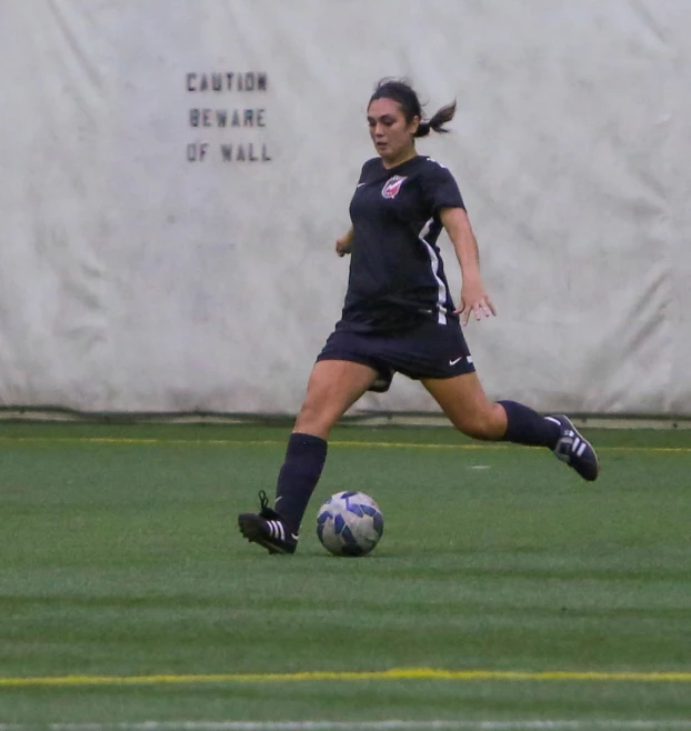 a woman in uniform kicking a soccer ball on a field