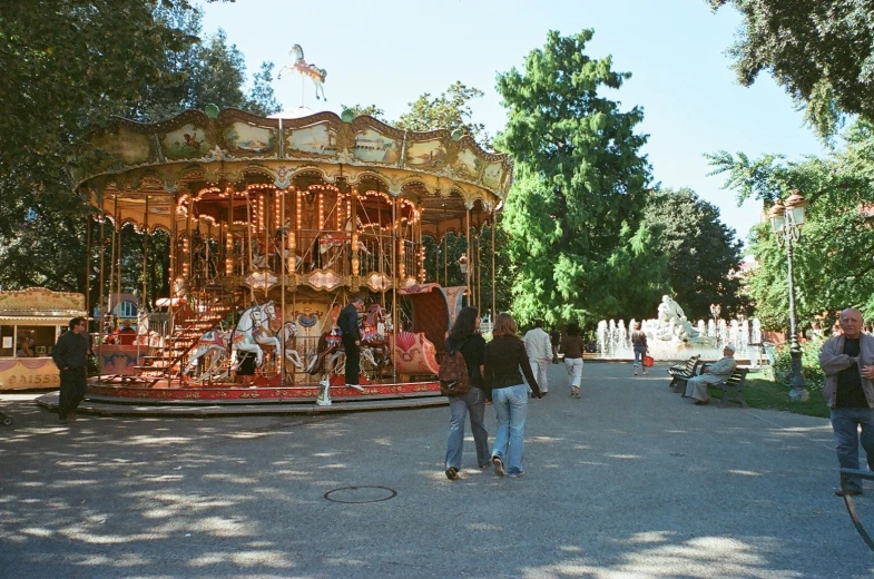 the carousel is surrounded by people walking and sitting on the other side of the road