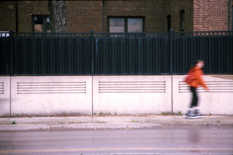 a person skateboarding along a city street near a fence