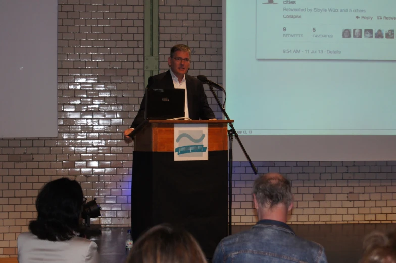 man speaking at podium in front of group of people