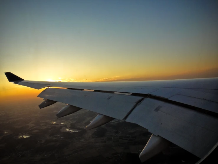 the wing of an airplane during sunset in the sky