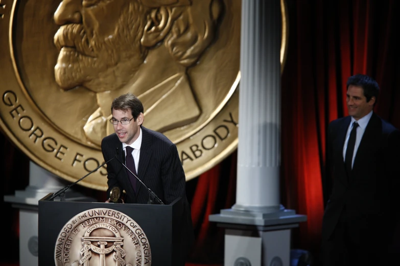 two men stand at podiums and speak to people