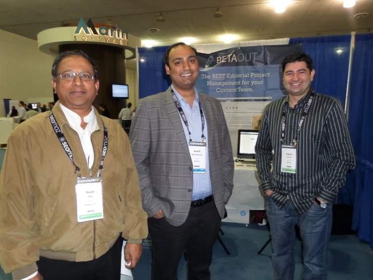 three men stand in front of an advertit for a company