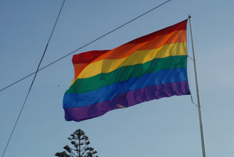 a rainbow colored flag flies against a blue sky
