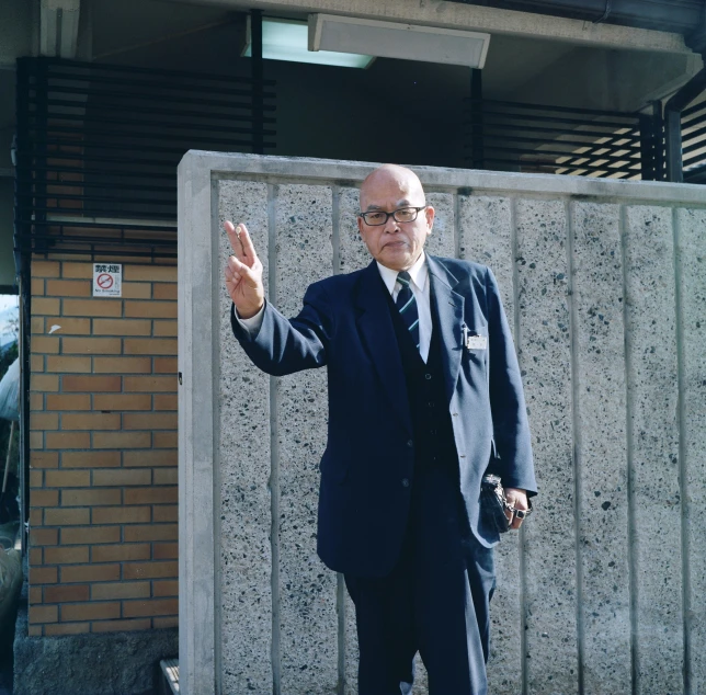 an old man in a business suit stands by a cement wall