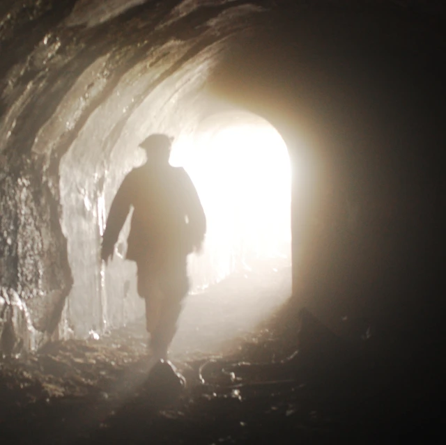 a man walking through a dark tunnel under a light