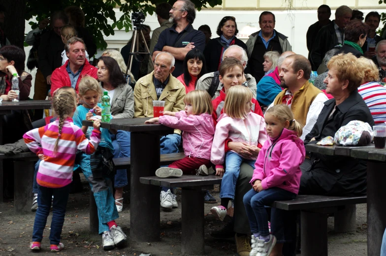 an image of people sitting on benches with other families around