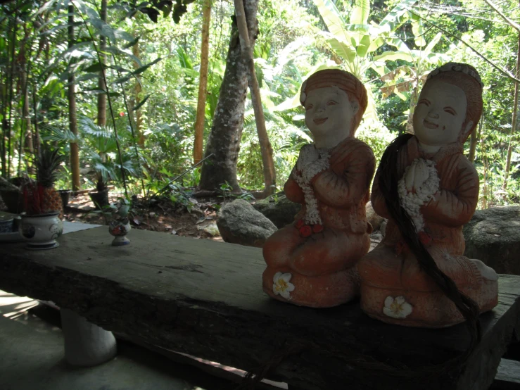 two small carved figurines sit on a wood beam