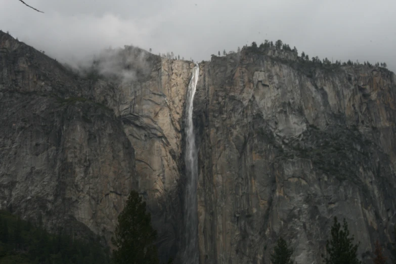 a waterfall near the top of mountains on a cloudy day