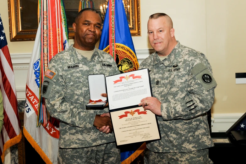 two service men in uniforms pose with an award