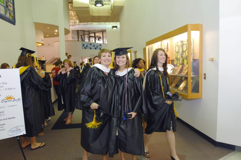 two girls in graduation gowns are smiling and standing in the hallway