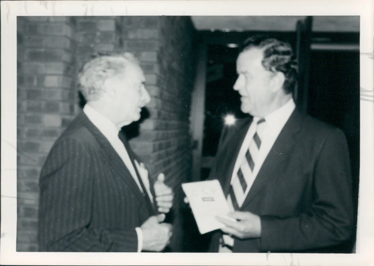 an old po shows a man in a suit and tie shaking hands with another man