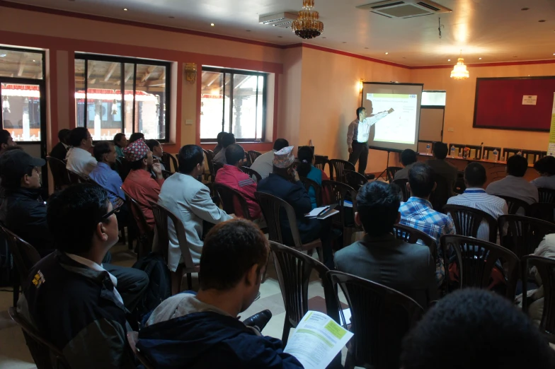 many people are sitting at chairs and one person is presenting