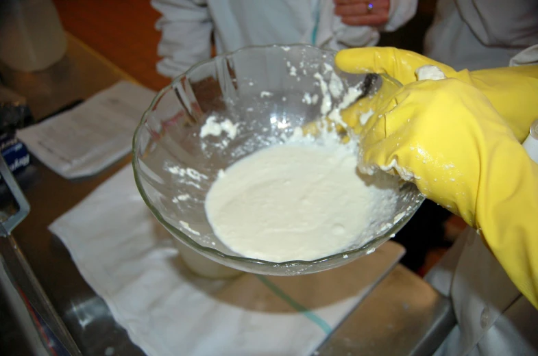 a person in yellow rubber gloves mixing food into a glass bowl