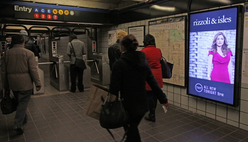 people are standing in front of a subway station with a large tv