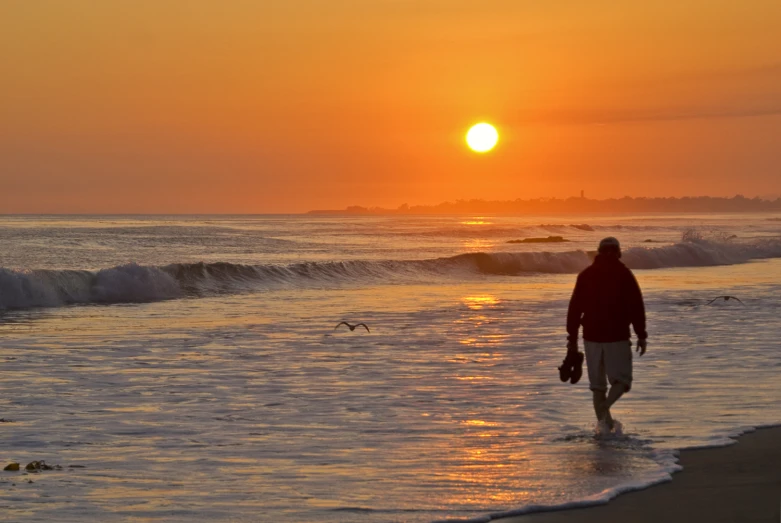 a person walking through the ocean at sunset