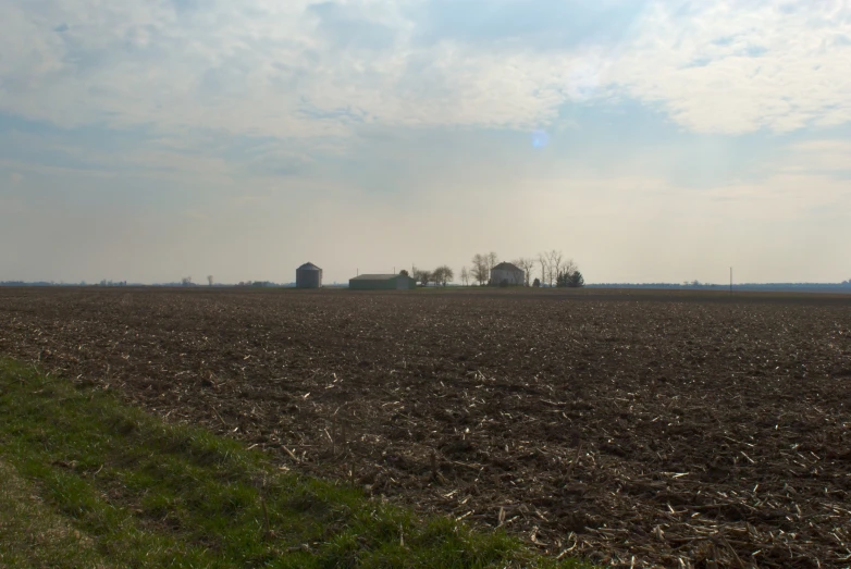 an open field and large farm buildings in the distance