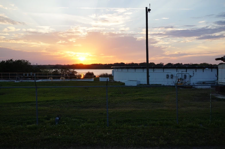 a barn sits near a body of water at sunset