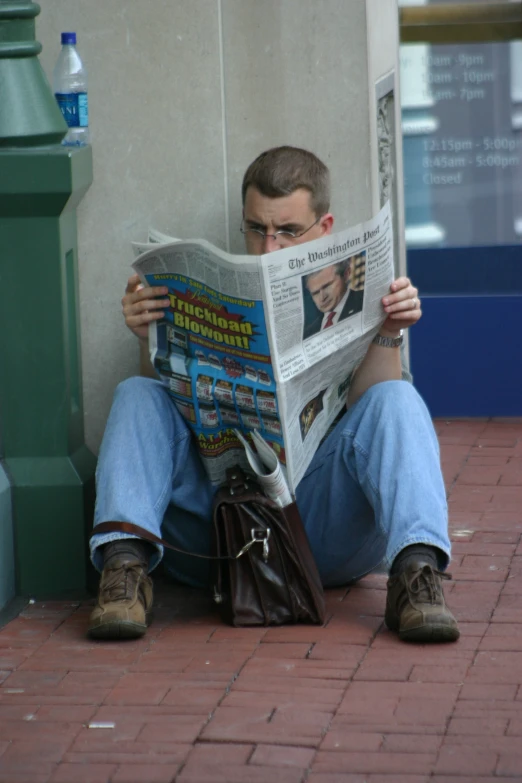 a man sitting on a city street reading a newspaper