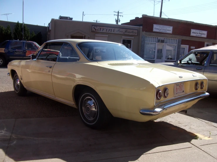 a yellow old car sits in front of a small business