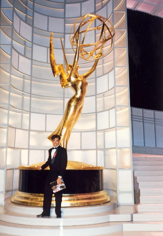 a man standing next to a giant gold award statue