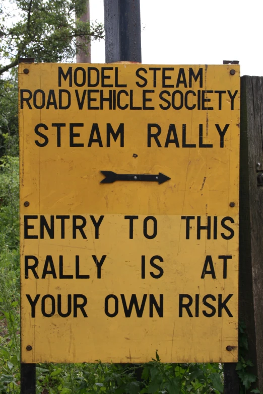 a yellow sign warning about steam railways next to an open field