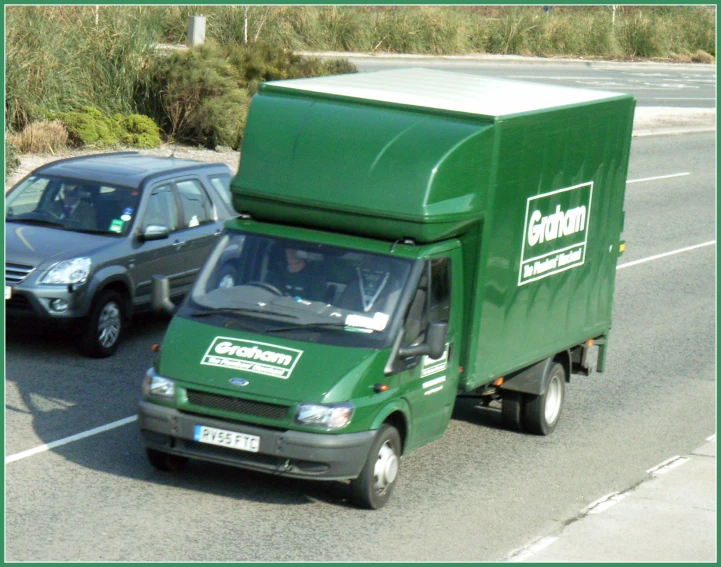a green delivery truck parked in front of a parked black car