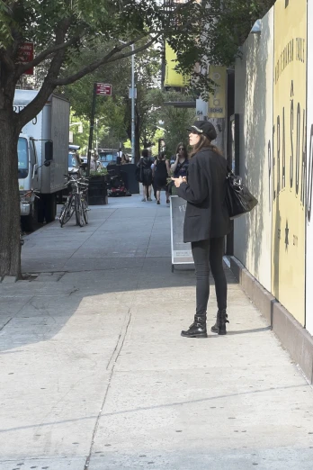 a woman on a sidewalk with a cellphone and a bag