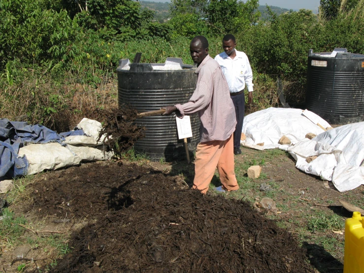 two people stand next to some water cans and dirt