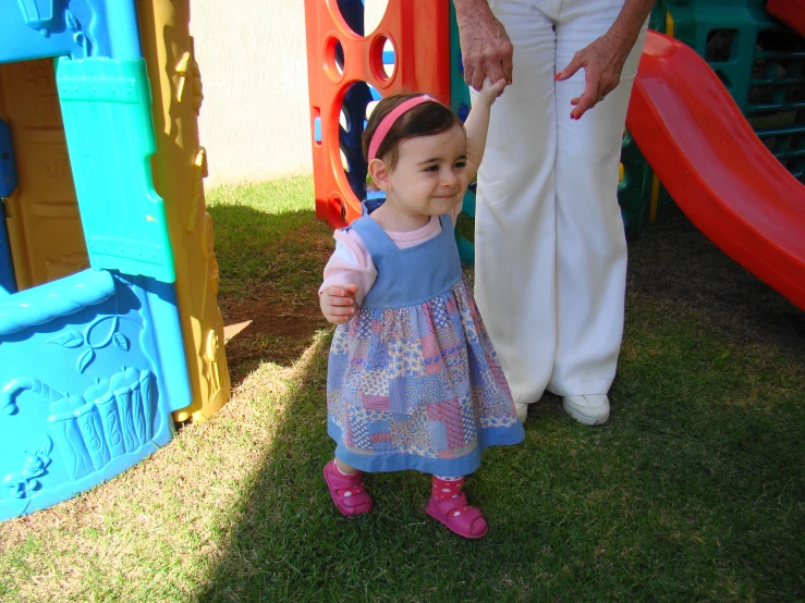 a little girl with pink shoes standing in front of a playground