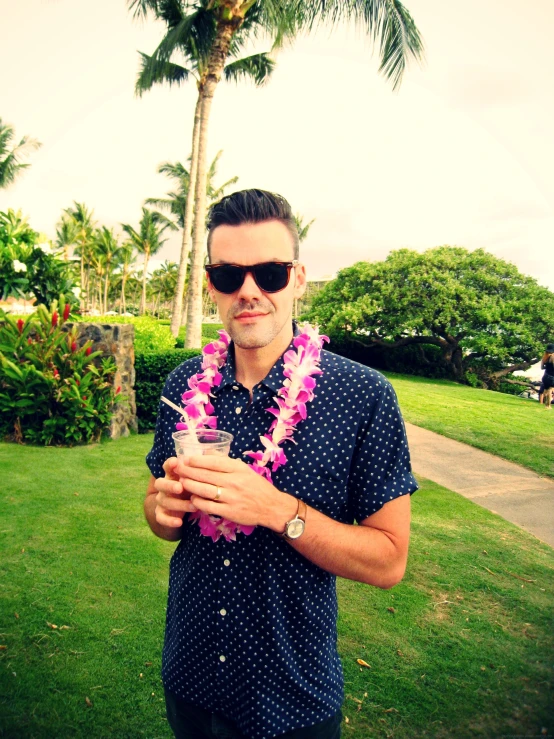 man wearing hawaiian lei holding a drink and posing for the camera