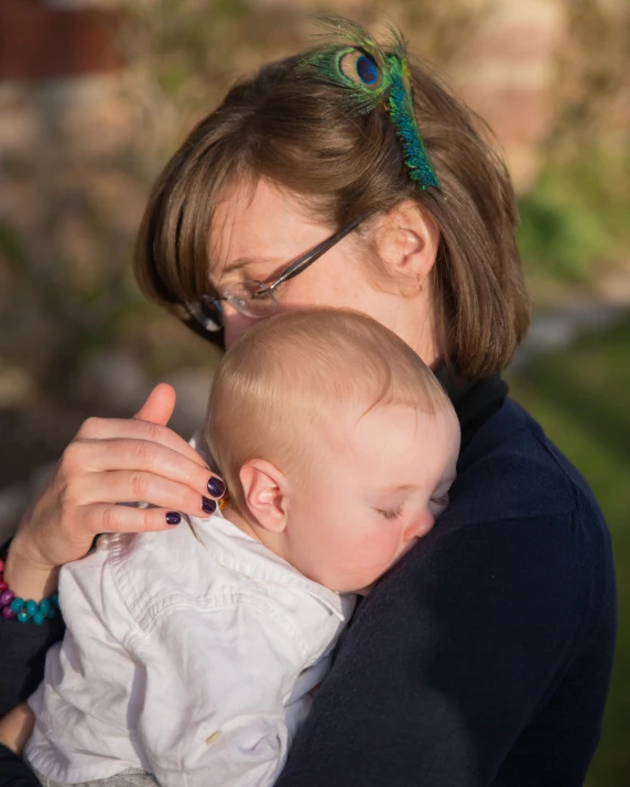 a lady holding a baby and kissing it with the eye of an owl on her shoulder