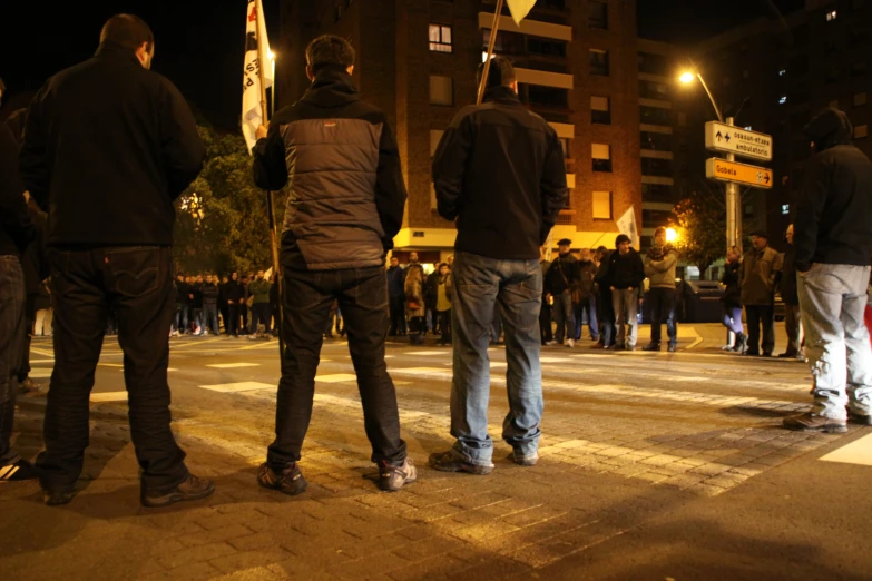 men stand on the sidewalk in front of an intersection at night