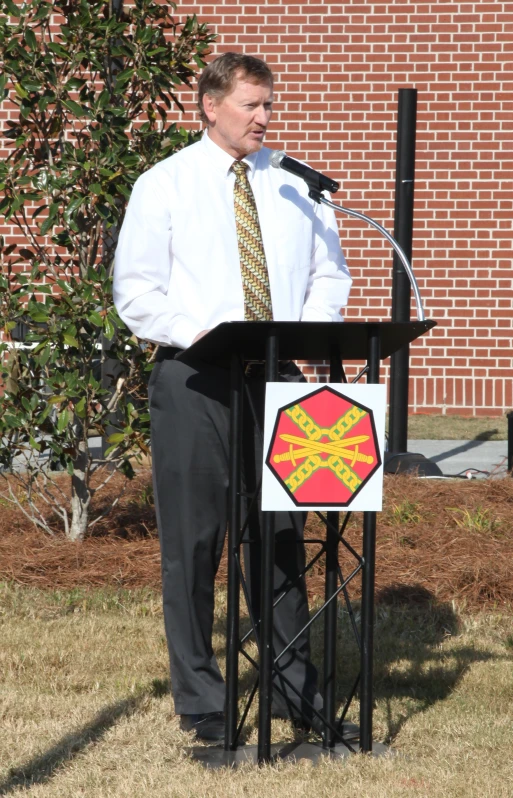 man standing at podium wearing white shirt and tie